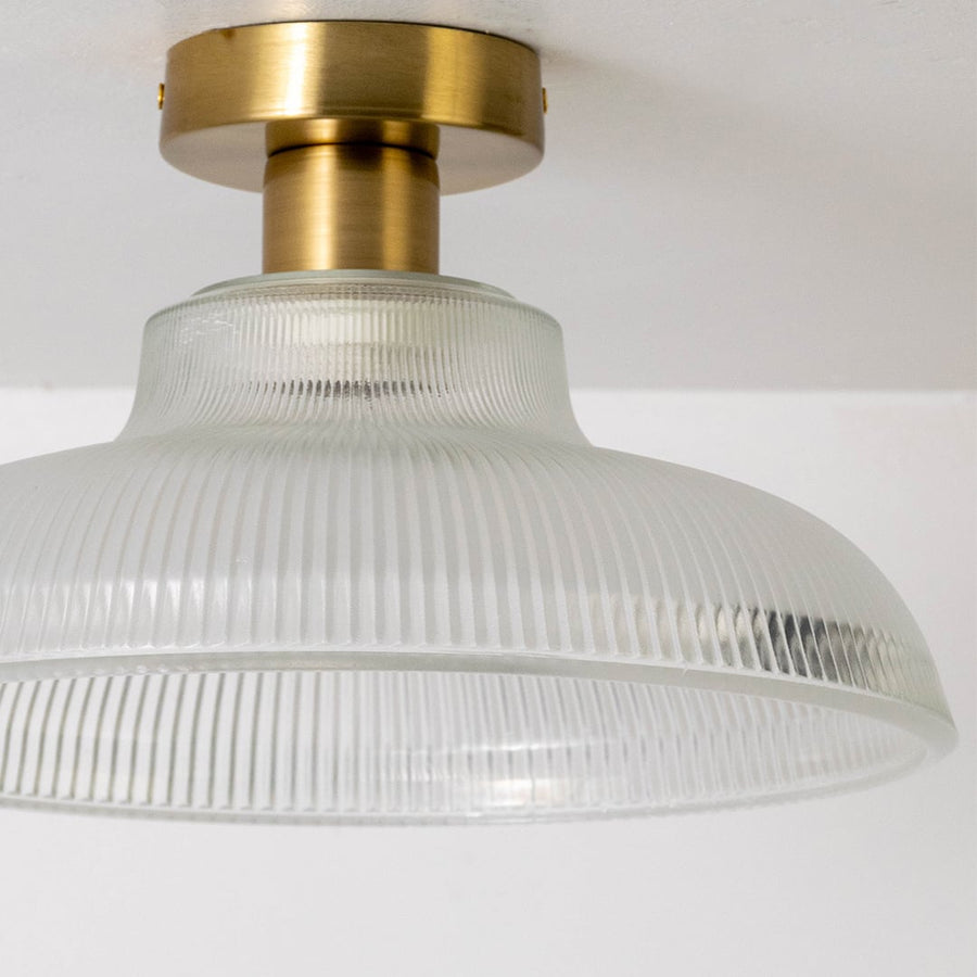 Close-up of clear ribbed glass ceiling light gold metal fixture showcasing detailed design and elegant lighting.