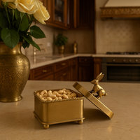 Gold square box with rabbit lid filled with cashews on a marble kitchen counter next to a vase of white roses for elegant home decor.