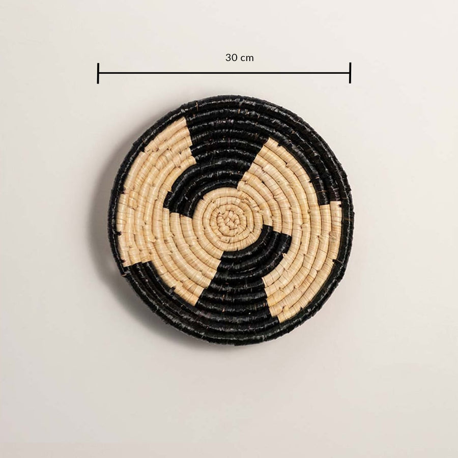 A handwoven natural and black rattan wall decor plate displayed on a white background clearly showing a diameter of 30 cm for accurate measurement and wall placement.