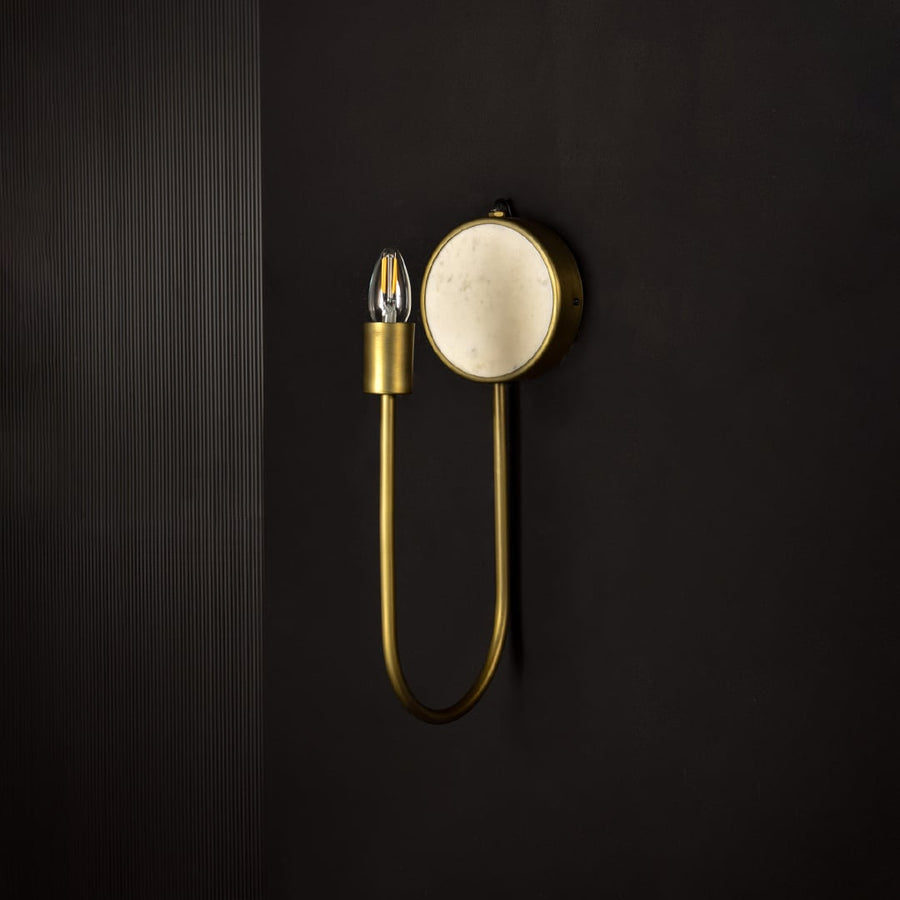 Metal and marble wall light shown unlit on dark background emphasizing minimalist design and golden finish for luxurious interior decor.
