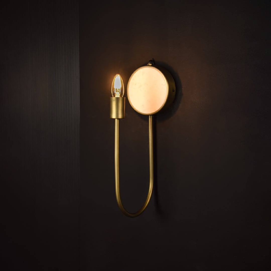 Modern brass wall light glowing on dark background showcasing marble base and elegant curve form creating depth in premium home decor.