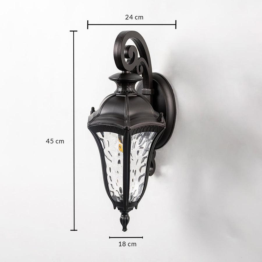 Lantern wall light dimensions 45 cm height 24 cm depth and 18 cm width feature an ornate black frame and clear textured glass.