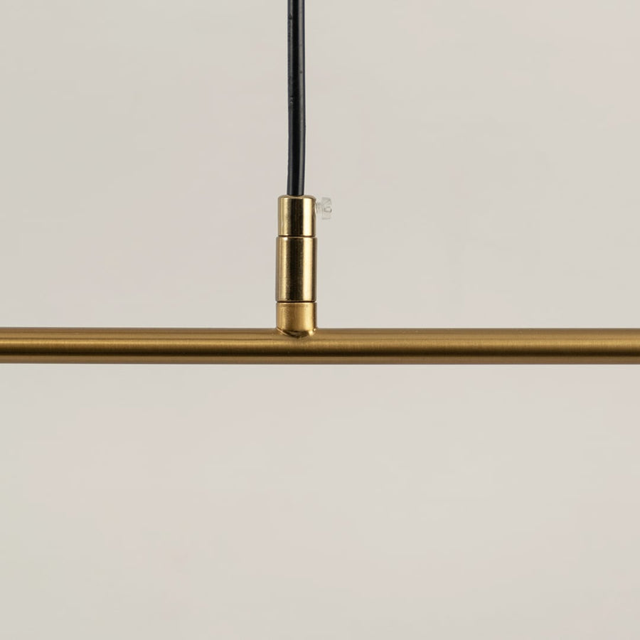Closeup of gold linear pendant light showing curved metal frame white diffuser tube and refined modern craftsmanship.
