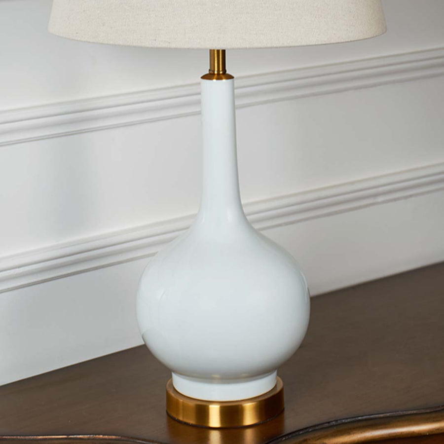 Closeup of ceramic lamp body with glossy white finish and gold detailing showing fine craftsmanship and smooth sculpted curves.