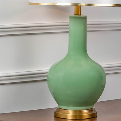 Closeup of green ceramic table lamp with glossy ceramic finish brass detailing and fabric shade for home decor.