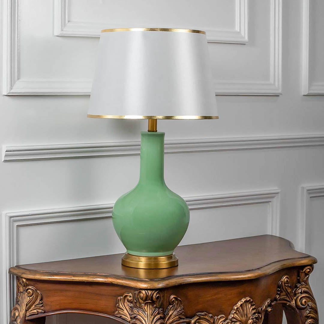 Green ceramic table lamp turned off with fabric shade and golden accents displayed on minimal white background.