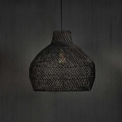 Handwoven black rattan pendant light against black background highlighting texture and craftsmanship of natural material.