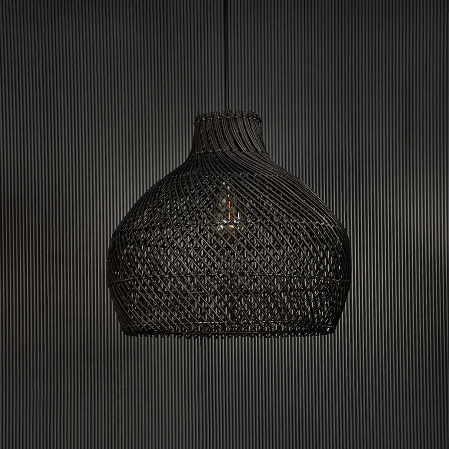 Handwoven black rattan pendant light against black background highlighting texture and craftsmanship of natural material.