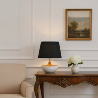 Black pleated table lamp on wooden console with classic wall paneling and floral decor for a sophisticated interior look.