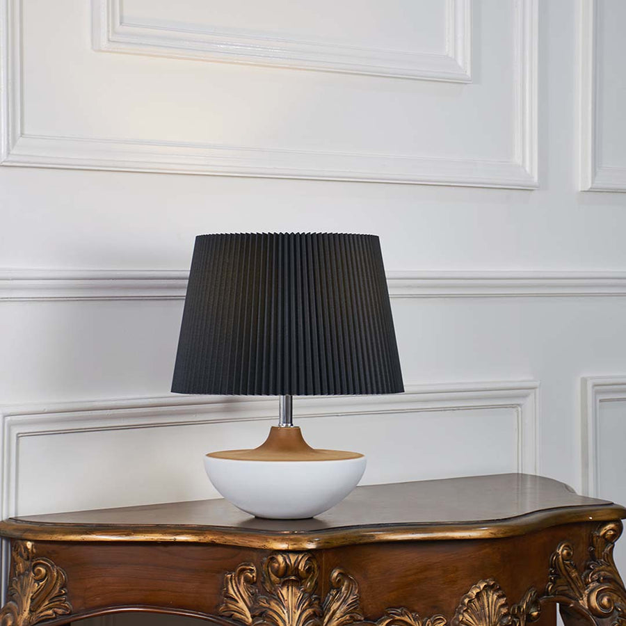Black fabric shade table lamp with white ceramic base and gold accent designed for elegant bedside and console decor.