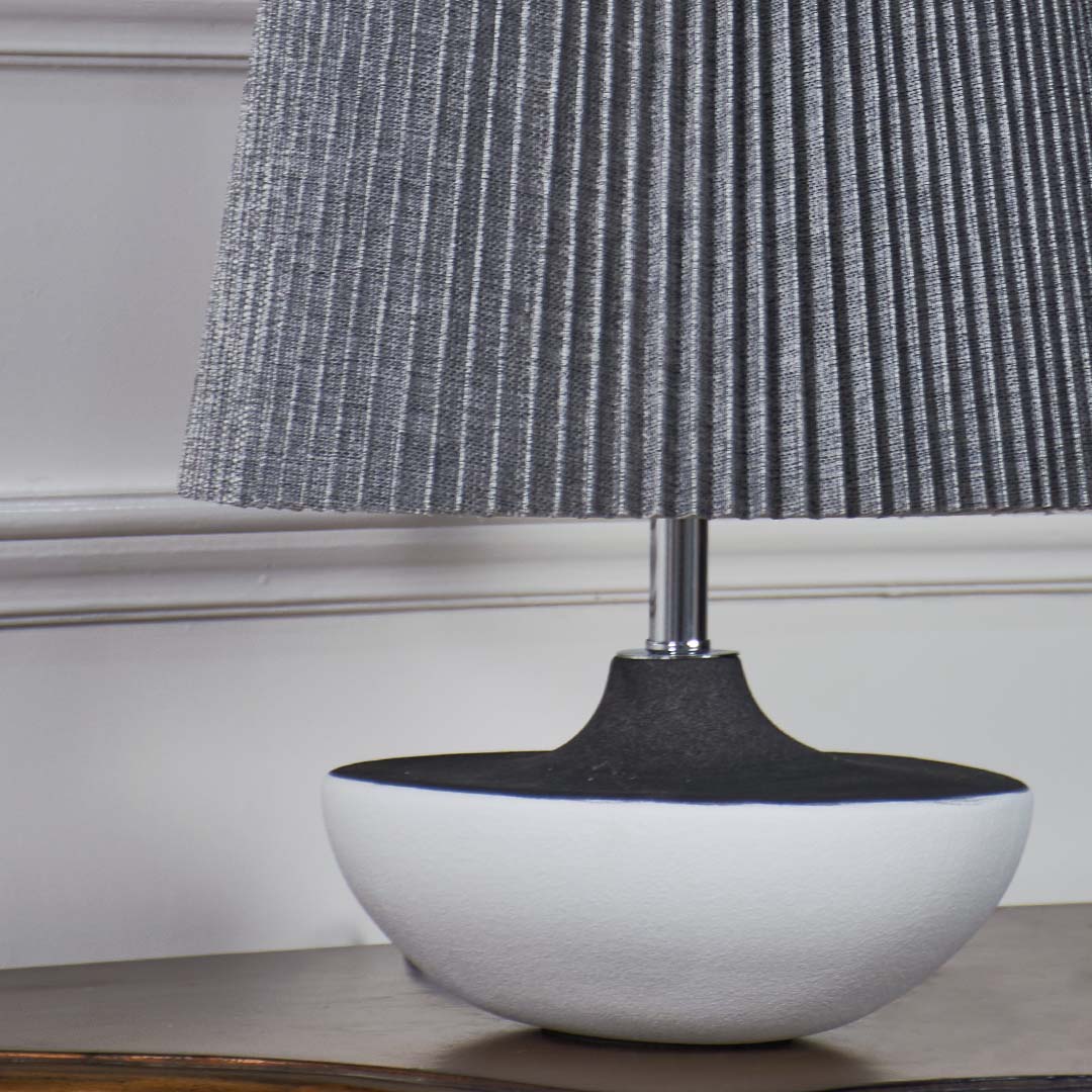 Closeup of grey pleated table lamp with smooth black and white ceramic base highlighting its elegant texture and contemporary design.