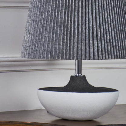 Closeup of grey pleated table lamp with smooth black and white ceramic base highlighting its elegant texture and contemporary design.