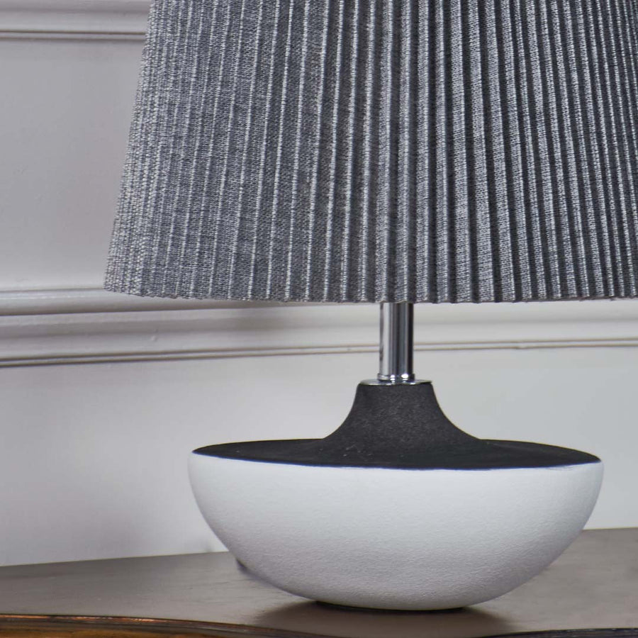 Closeup of grey pleated table lamp with smooth black and white ceramic base highlighting its elegant texture and contemporary design.
