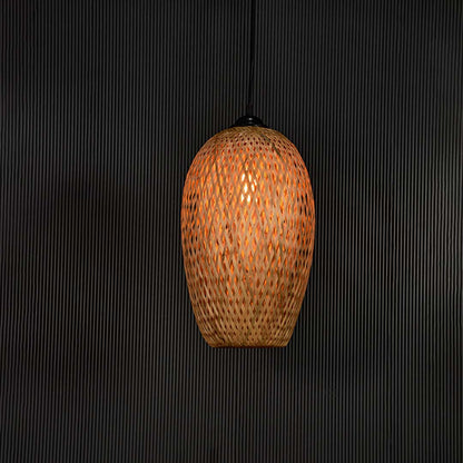 Woven bamboo pendant light glowing on black background with tall oval wicker shade for bohemian modern interiors.