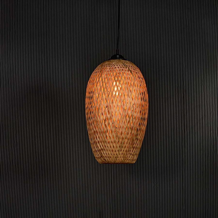 Woven bamboo pendant light glowing on black background with tall oval wicker shade for bohemian modern interiors.