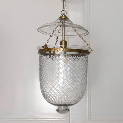 Pendant light featuring antique metal framework and clear textured glass shade suspended elegantly for indoor decor.