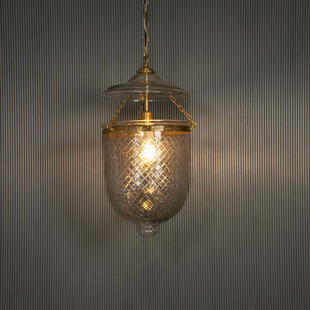 Textured clear glass pendant light with antique brass finish illuminated for vintage decor.