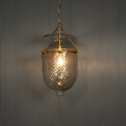 Textured clear glass pendant light with antique brass finish illuminated for vintage decor.