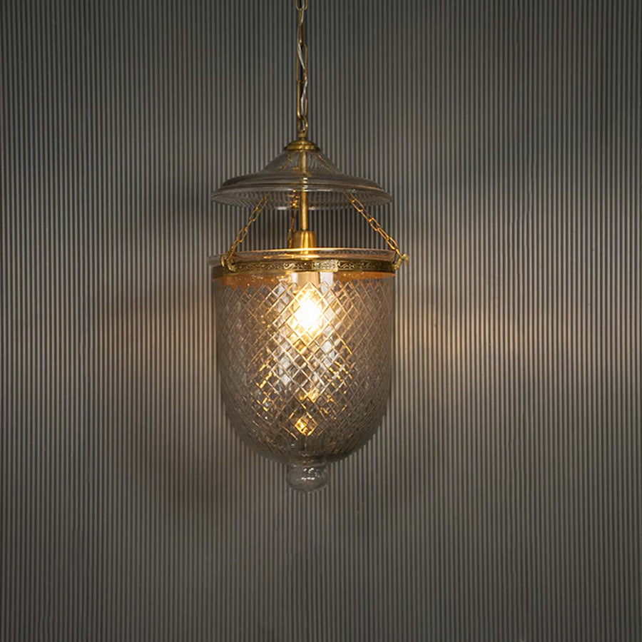 Textured clear glass pendant light with antique brass finish illuminated for vintage decor.