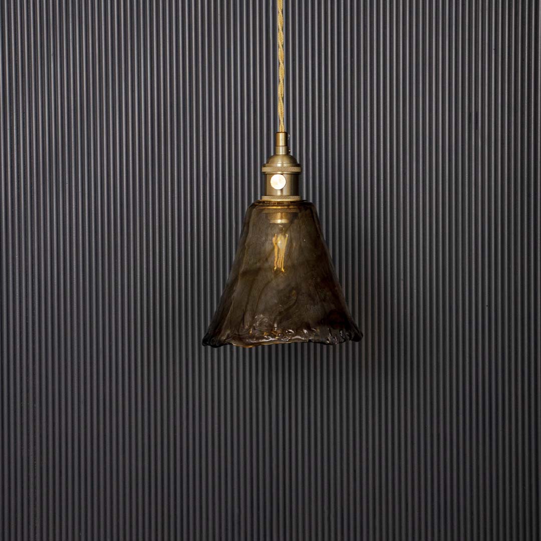 Wavy amber glass pendant lamp with brass holder displayed off on black background adding style to modern interiors.