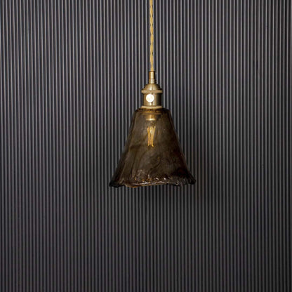 Wavy amber glass pendant lamp with brass holder displayed off on black background adding style to modern interiors.