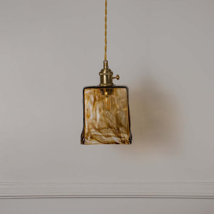 Decorative amber marbled glass pendant light with brass accents designed for stylish living spaces.