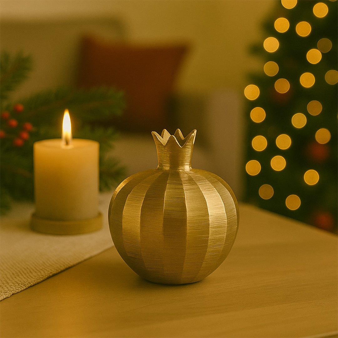 Warm festive setting showcasing a golden pomegranate decor placed on a wooden table with a glowing candle and softly lit Christmas tree in the background.