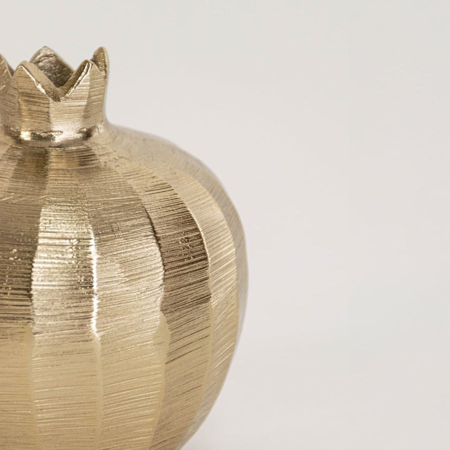 Close view of gold metal pomegranate sculpture highlighting crown detailing and rich hammered finish texture