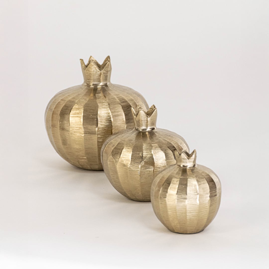 Small gold pomegranate sculpture featured in cozy home decor setting ideal for festive or elegant shelf accents