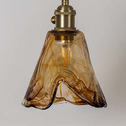 Amber glass pendant light with wavy sculpted shade and gold fittings placed against neutral wall background showcasing warm decorative lighting appeal.
