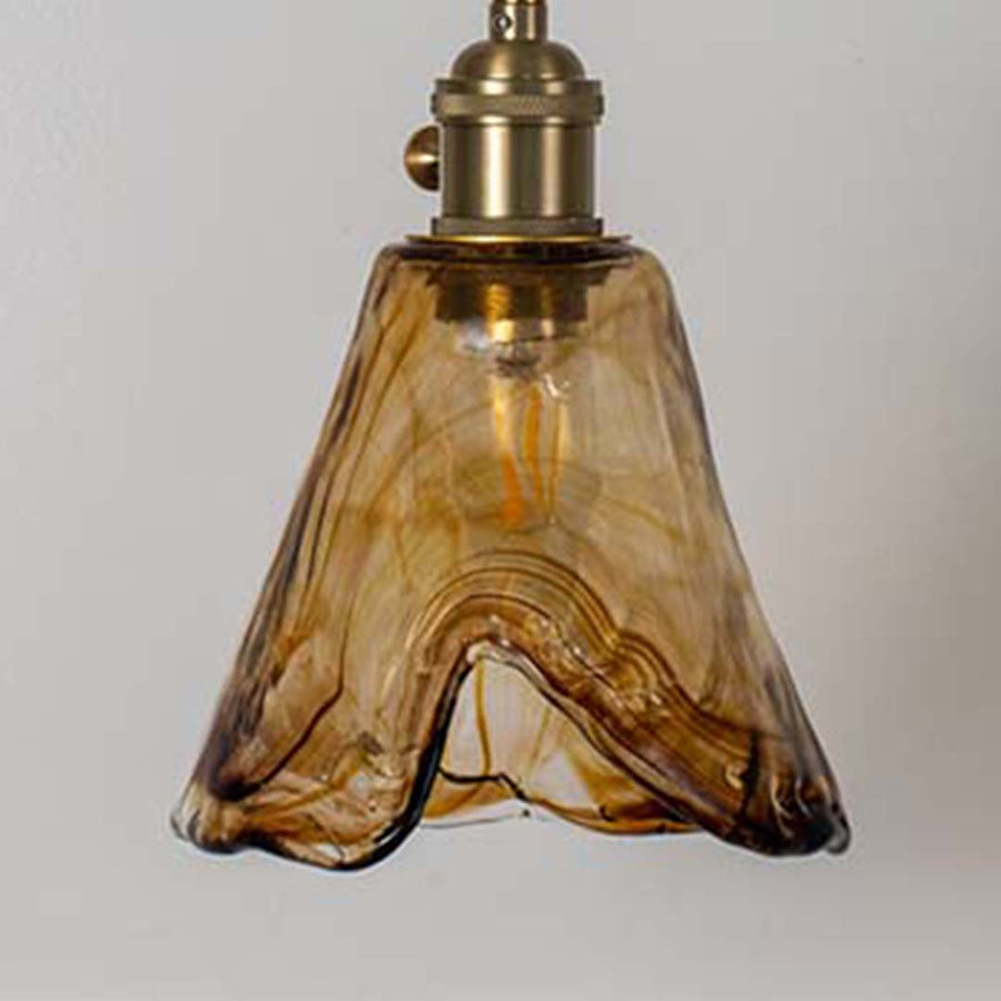 Amber glass pendant light with wavy sculpted shade and gold fittings placed against neutral wall background showcasing warm decorative lighting appeal.