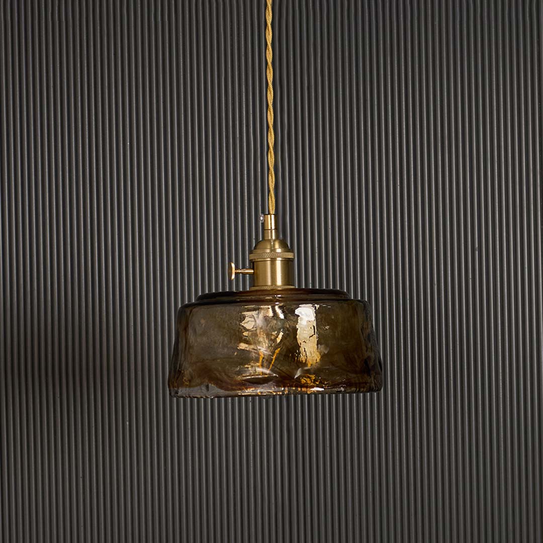 Amber glass pendant light turned off against black background displaying vintage industrial shade with brass fitting hardware.