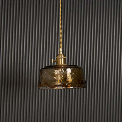 Amber glass pendant light turned off against black background displaying vintage industrial shade with brass fitting hardware.