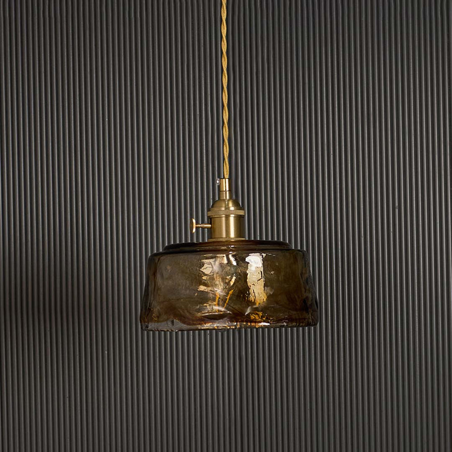 Amber glass pendant light turned off against black background displaying vintage industrial shade with brass fitting hardware.