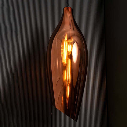 A bronze sculpted glass pendant light with lights on casting a warm glow on a dark backdrop showcasing its tall curved silhouette.