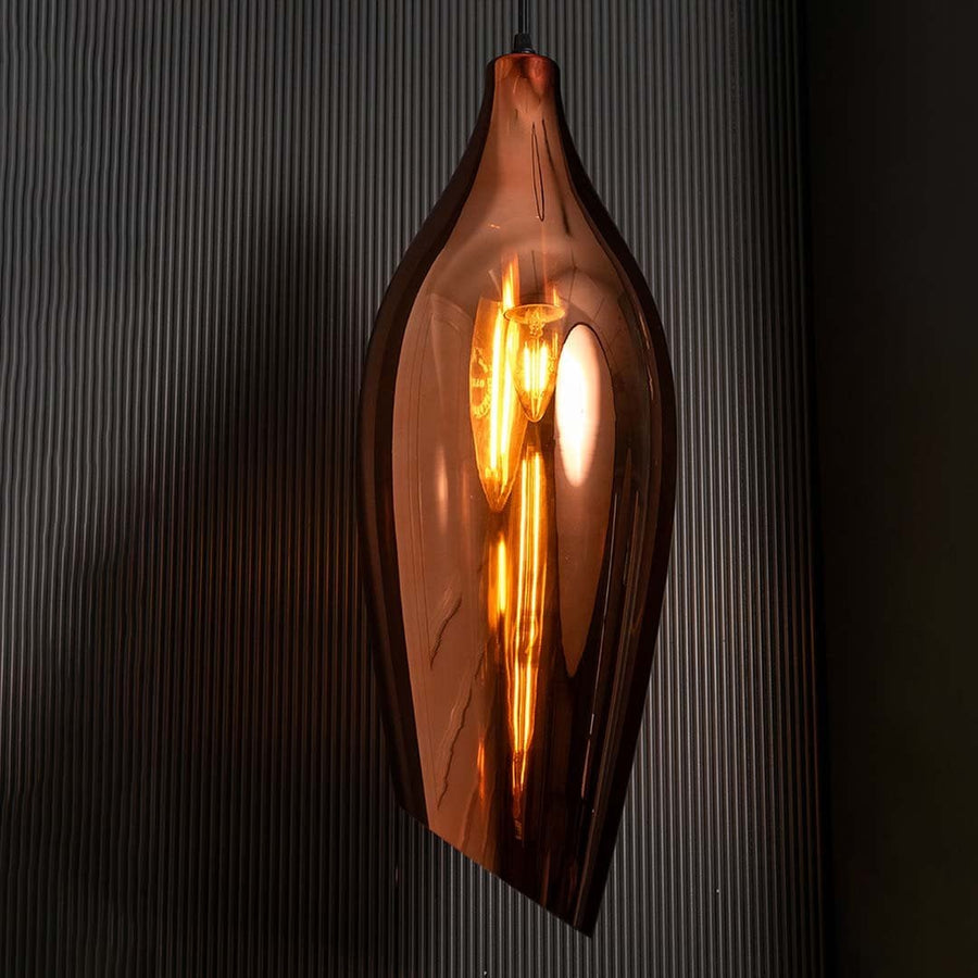 A bronze sculpted glass pendant light with lights on casting a warm glow on a dark backdrop showcasing its tall curved silhouette.