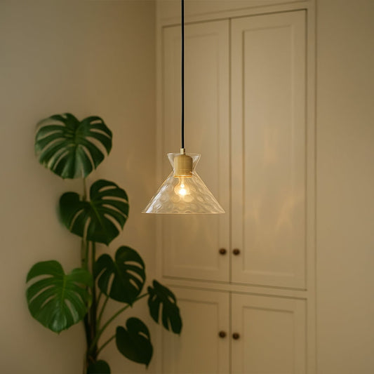 Clear conical glass pendant light with wooden holder hanging above table adding warm glow to stylish home interiors.