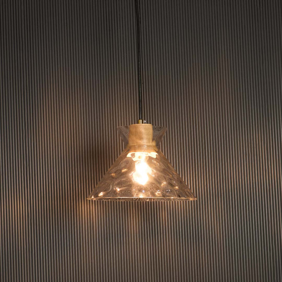 Clear glass pendant light with wooden holder glowing warmly against black background for premium home lighting.