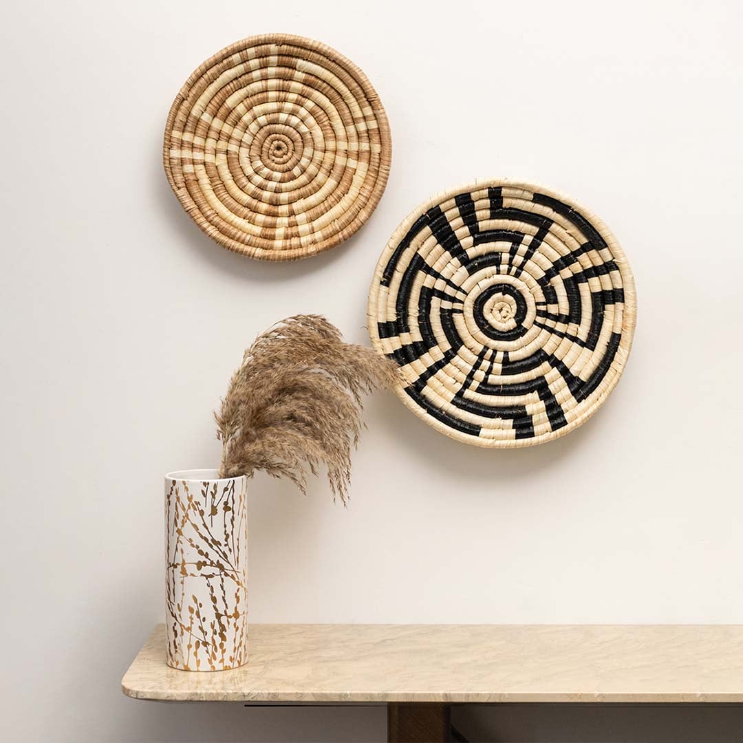 A grouped display of two natural rattan wall decor plates on a white wall with a tall vase creating a warm handcrafted accent for earthy rustic home styling.