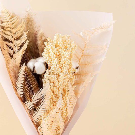 An elegant beige dried floral bouquet with white cotton pods and preserved fern leaves wrapped for minimalist rustic decor.