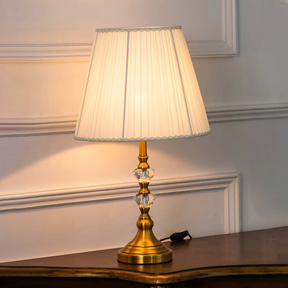 Clear crystal table lamp with pleated fabric shade creating elegant classic ambient lighting for luxury interior spaces.