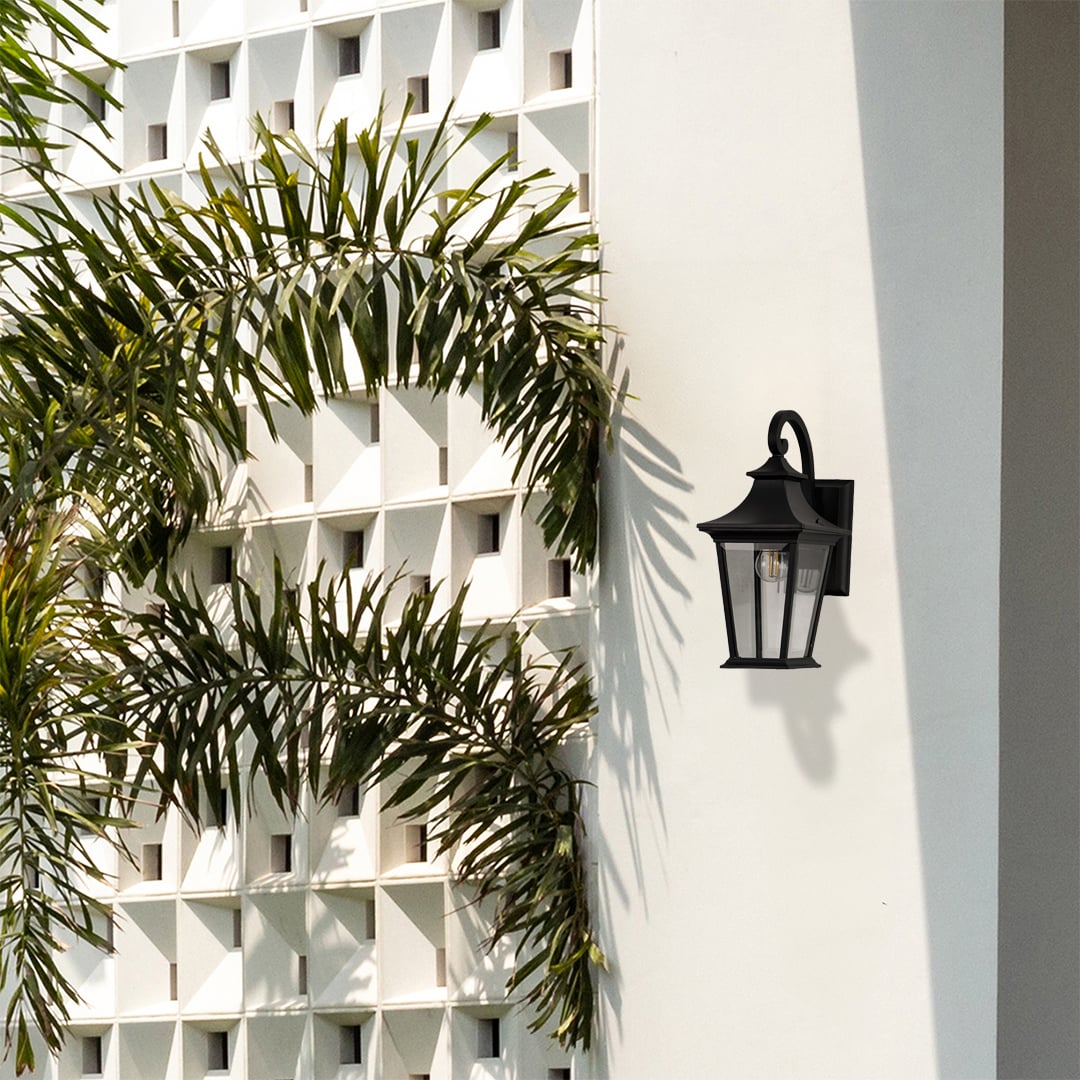 Elegant black metal outdoor wall lantern with clear glass panels adding warm lighting to entrance and patio walls.