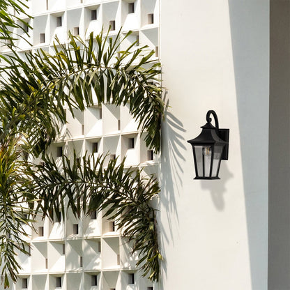 Elegant black metal outdoor wall lantern with clear glass panels adding warm lighting to entrance and patio walls.