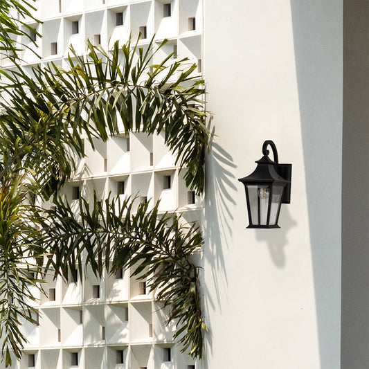 Elegant black metal outdoor wall lantern with clear glass panels adding warm lighting to entrance and patio walls.