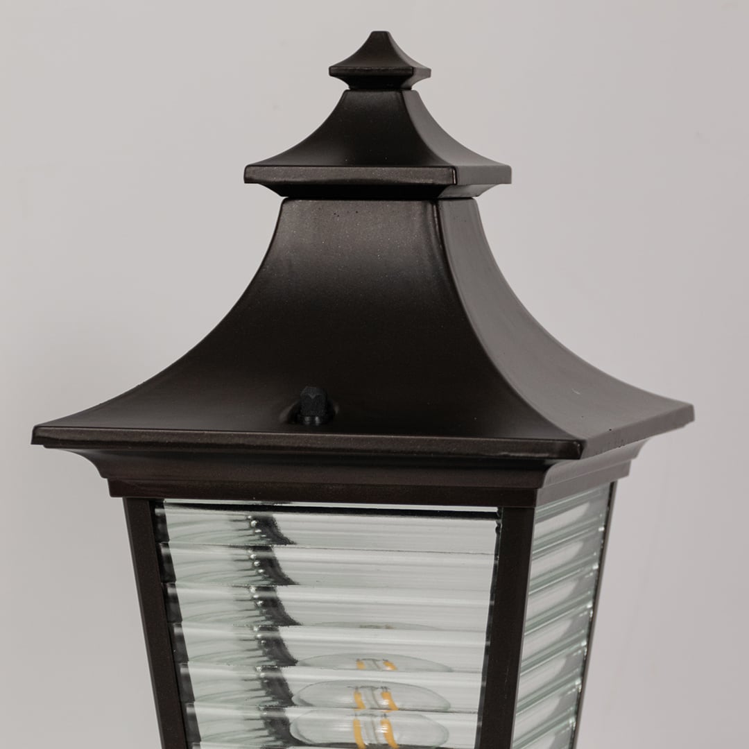 Closeup view of black metal pillar light with ribbed glass body highlighting its detailing for outdoor home lighting.
