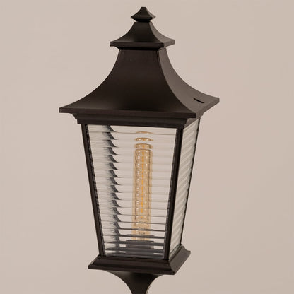 Closeup of black metal pillar lamp with detailed ribbed glass and warm bulb highlighting premium outdoor design.