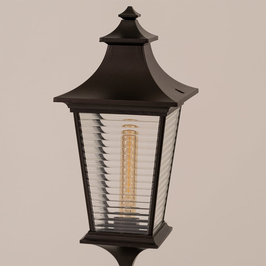 Closeup of black metal pillar lamp with detailed ribbed glass and warm bulb highlighting premium outdoor design.