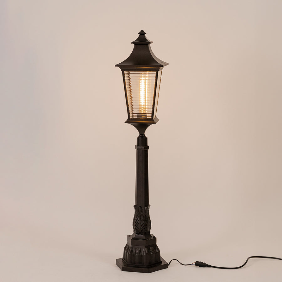Vintage black outdoor garden light with warm glowing ribbed panels for elegant exterior decor use.