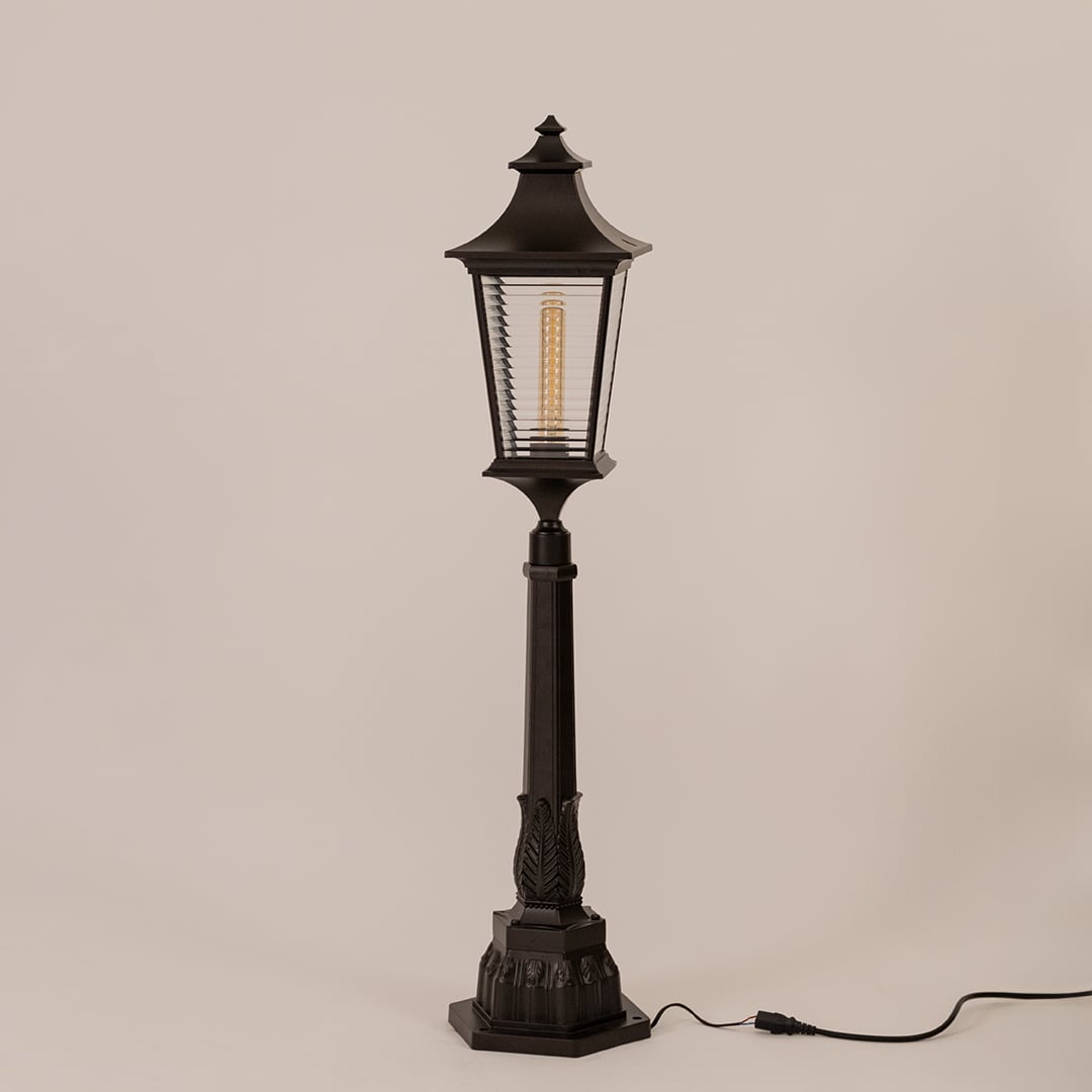 Black outdoor pillar lamp with clear ribbed glass and metal frame displayed on white background with bulb off.