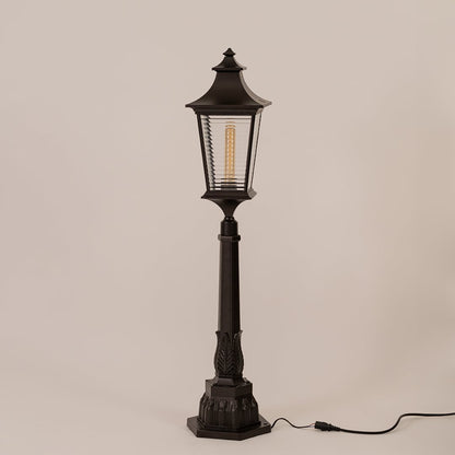 Black outdoor pillar lamp with clear ribbed glass and metal frame displayed on white background with bulb off.
